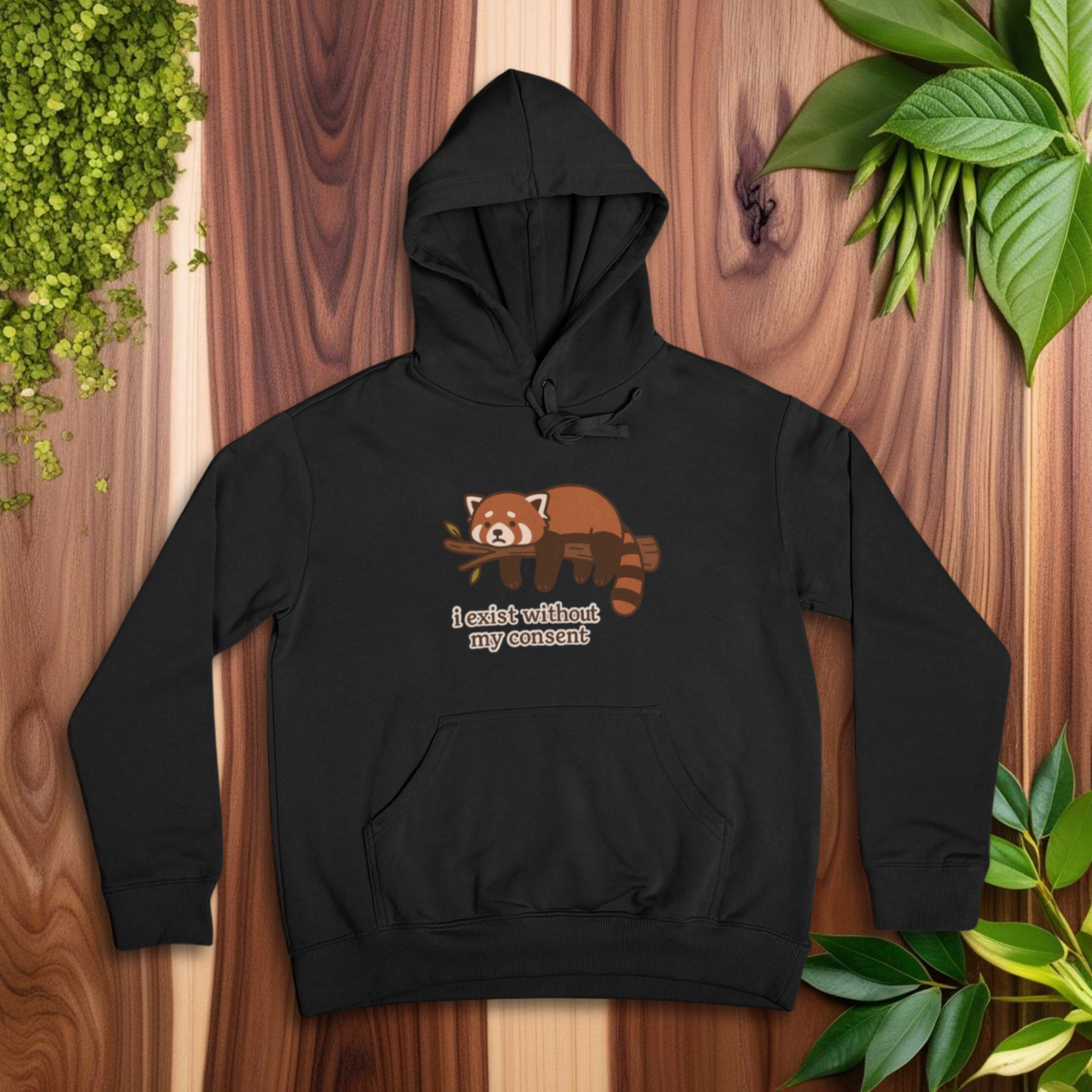 Black hoodie with a red panda design on a wooden surface with plants around